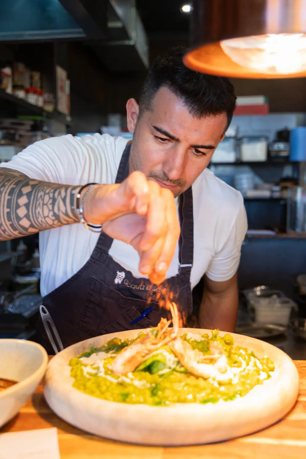Chef seasoning a prawn risotto plate in the Acqua e Sale kitchen