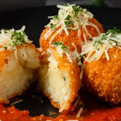 Crispy arancini balls filled with melted cheese and topped with parmesan and herbs, plated on a bed of tomato sauce in a professional food photography setup in Perth.
