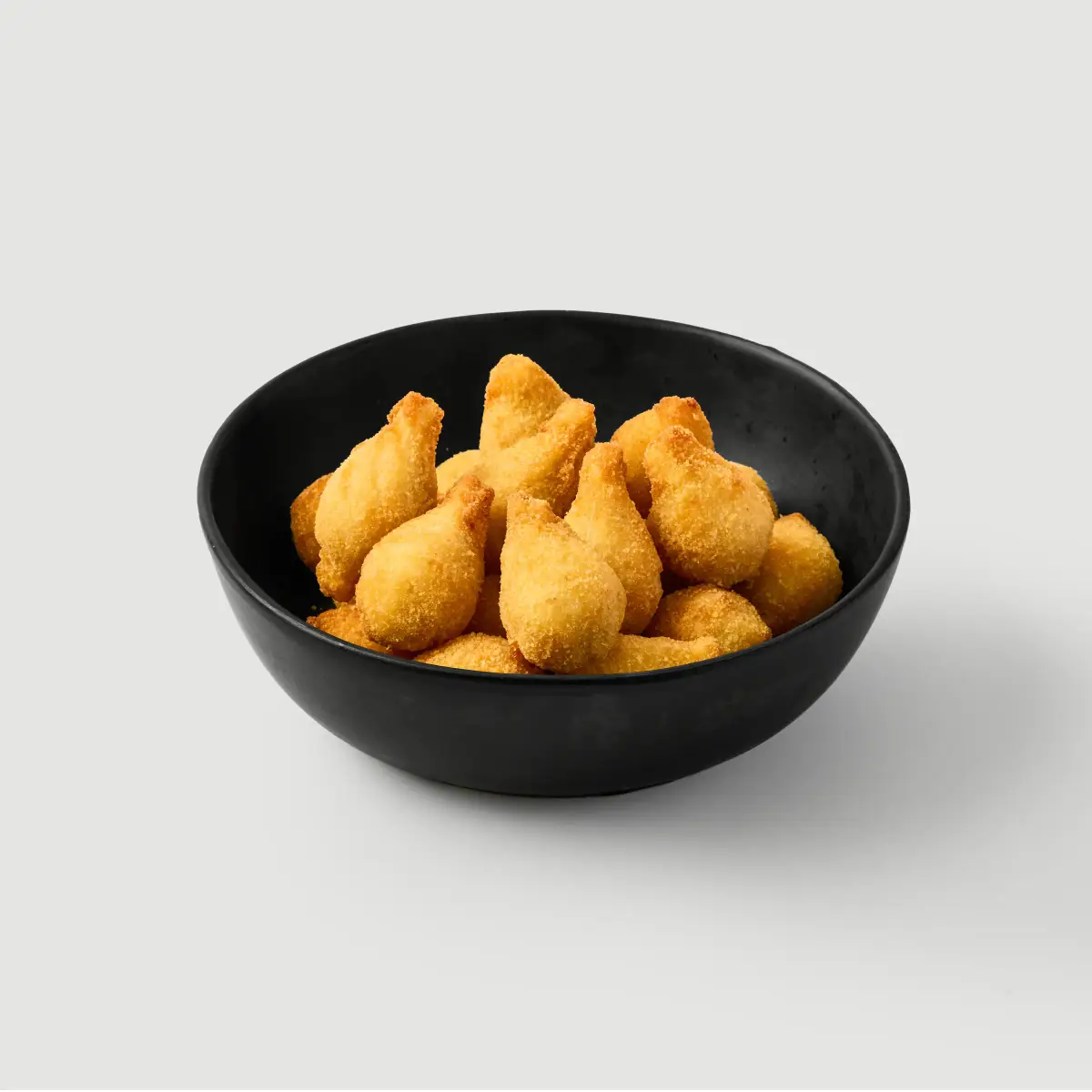 Crumbed arancini snack bites in a black bowl photographed against a clean white background