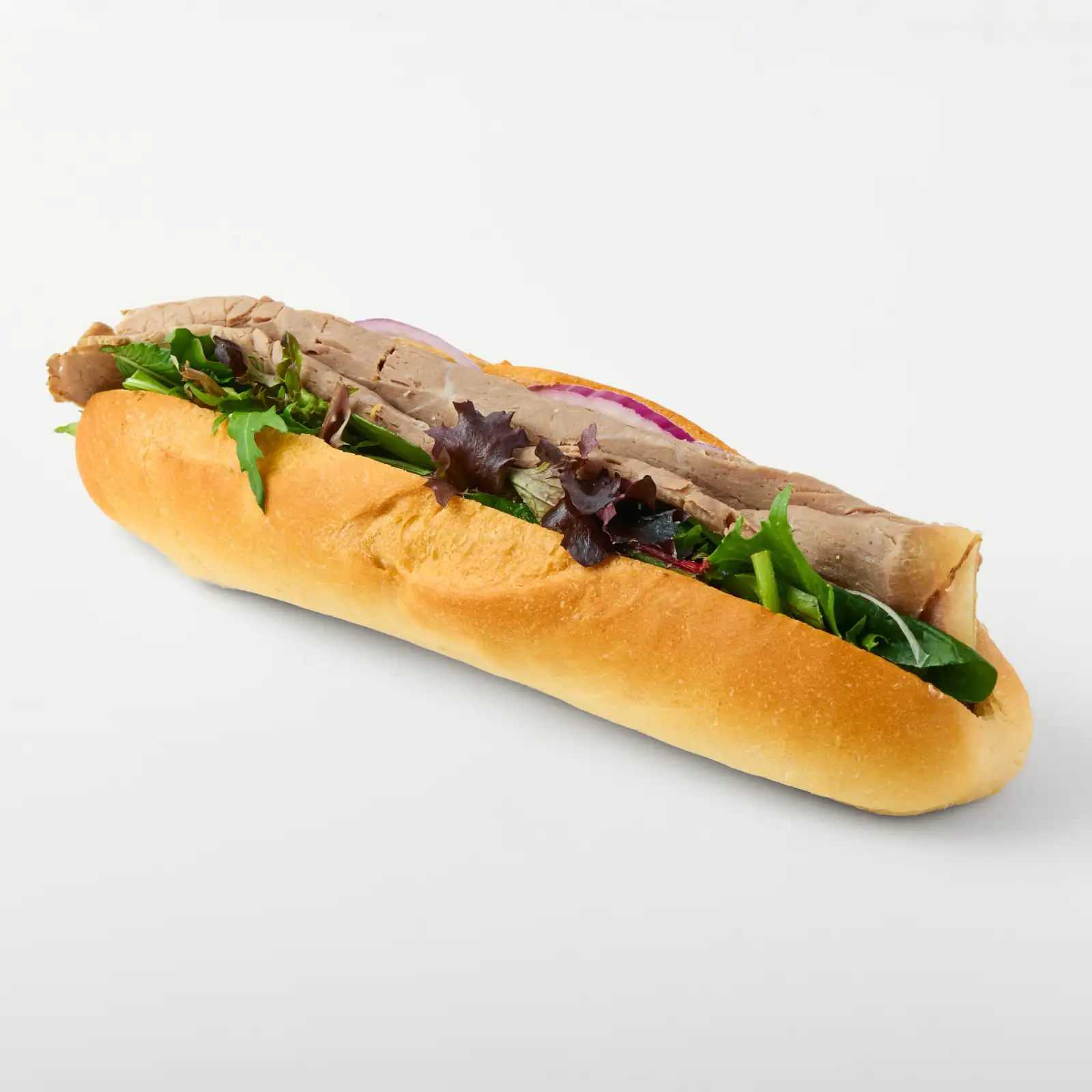 Filled baguette with salad leaves, sliced protein and red onion photographed against a clean white background