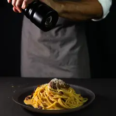 Chef grinding fresh pepper over a plate of spaghetti carbonara, photographed in an action-style restaurant food photography scene in Perth.