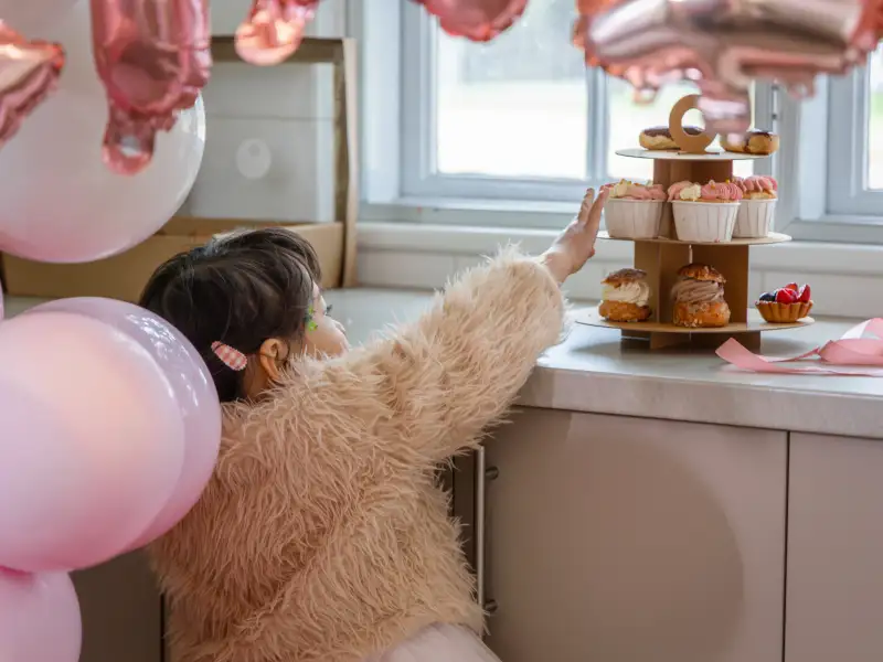 Child reaching toward a cupcake stand during a birthday celebration.