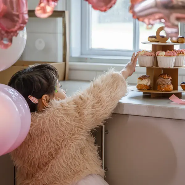 Child reaching toward a cupcake stand during a birthday celebration.
