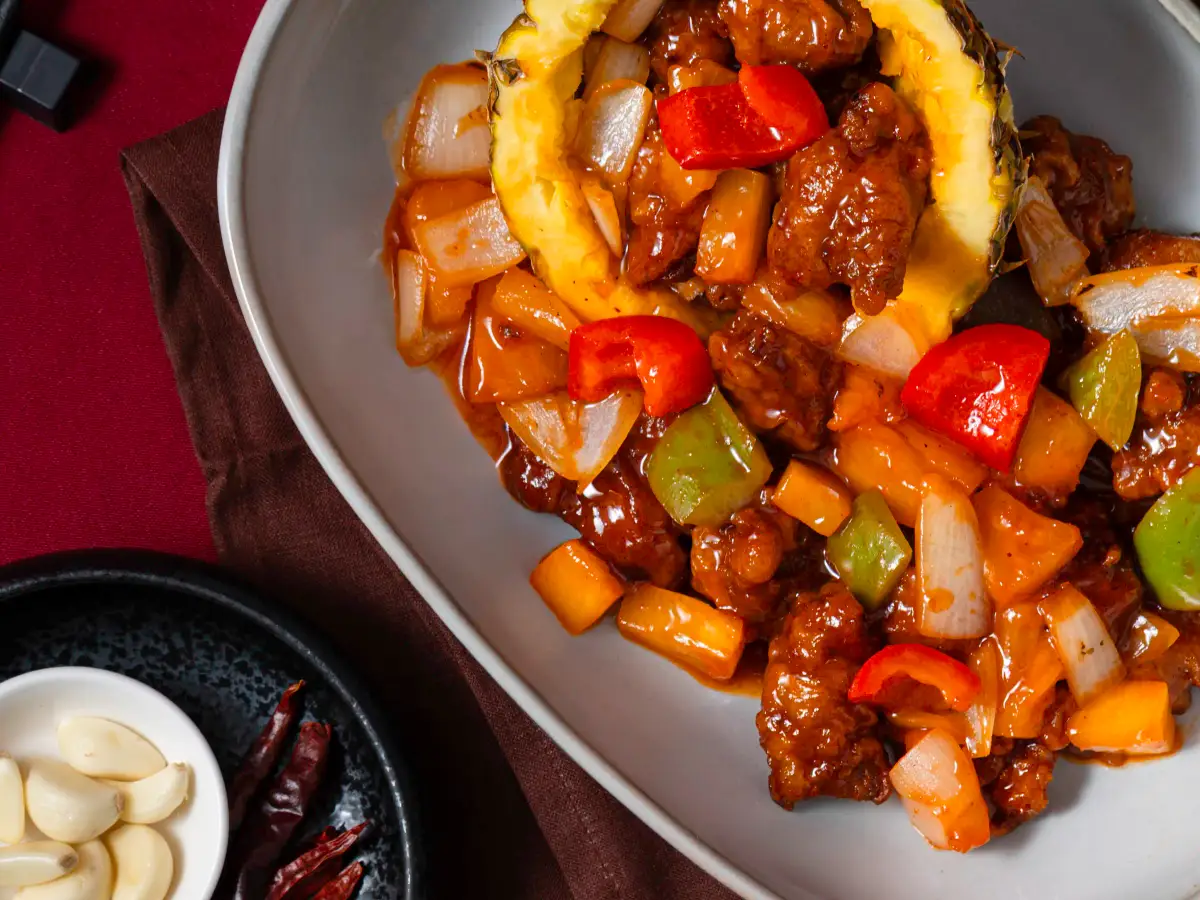 Overhead view of pineapple bowl stir-fry with chopsticks, tea, dried chillies, and garlic on a red backdrop at Como Garden Restaurant