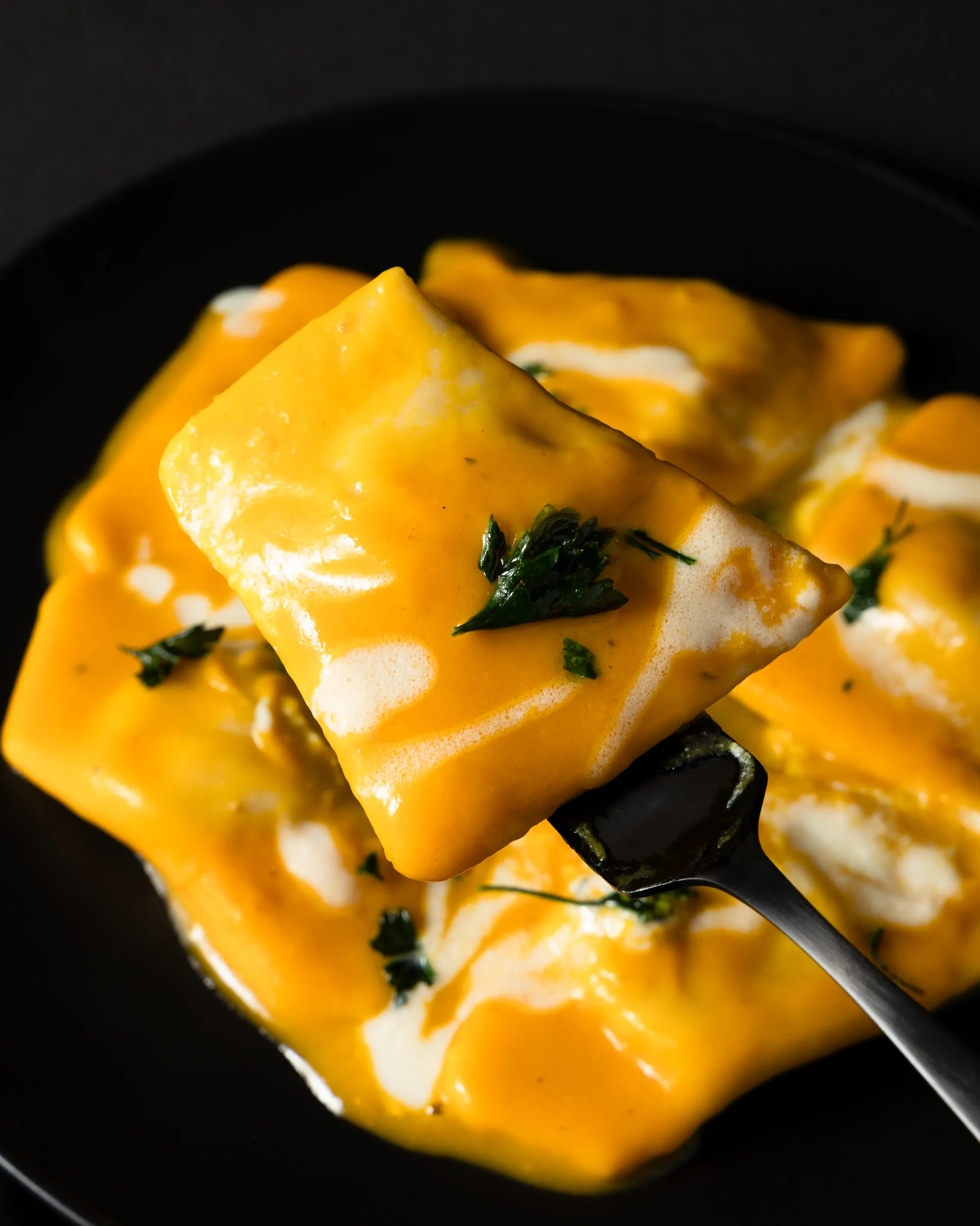 Creamy ravioli pasta close up with herbs on a black plate