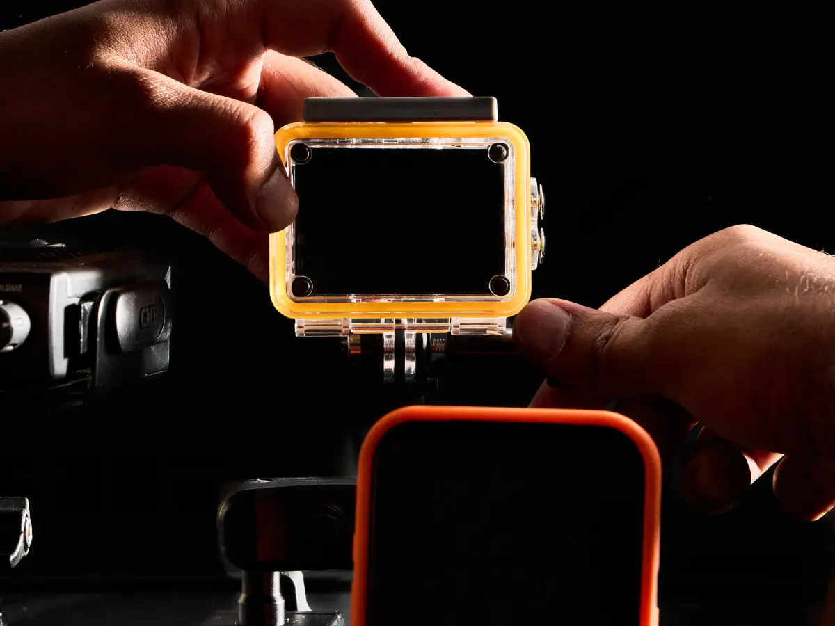 Hands holding the orange-edged action camera housing attached to a Duravilk dashboard mounting setup