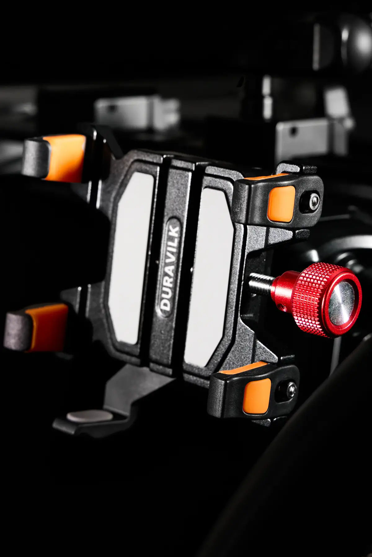 Angled view of a black Duravilk device holder with visible branding, orange contact pads and a red adjustment knob