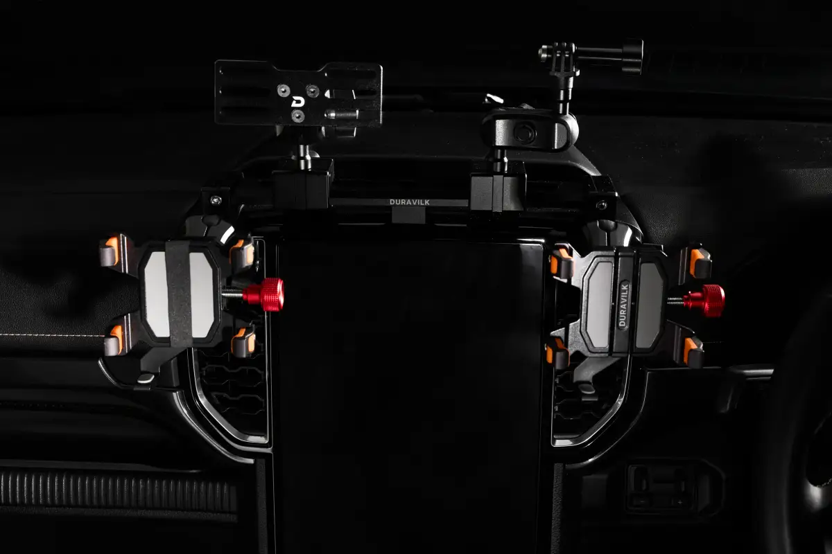 Wide view of a Duravilk rail installed above a vehicle display with two device holders, orange contact pads and red adjustment knobs