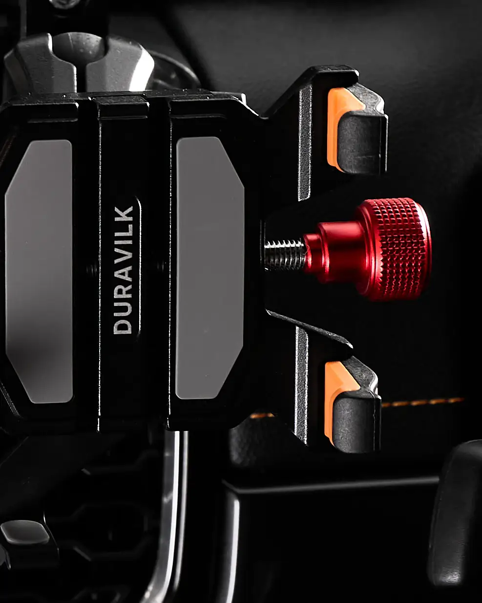 Side detail of a Duravilk device holder showing the branded face, orange contact pads and threaded red adjustment knob