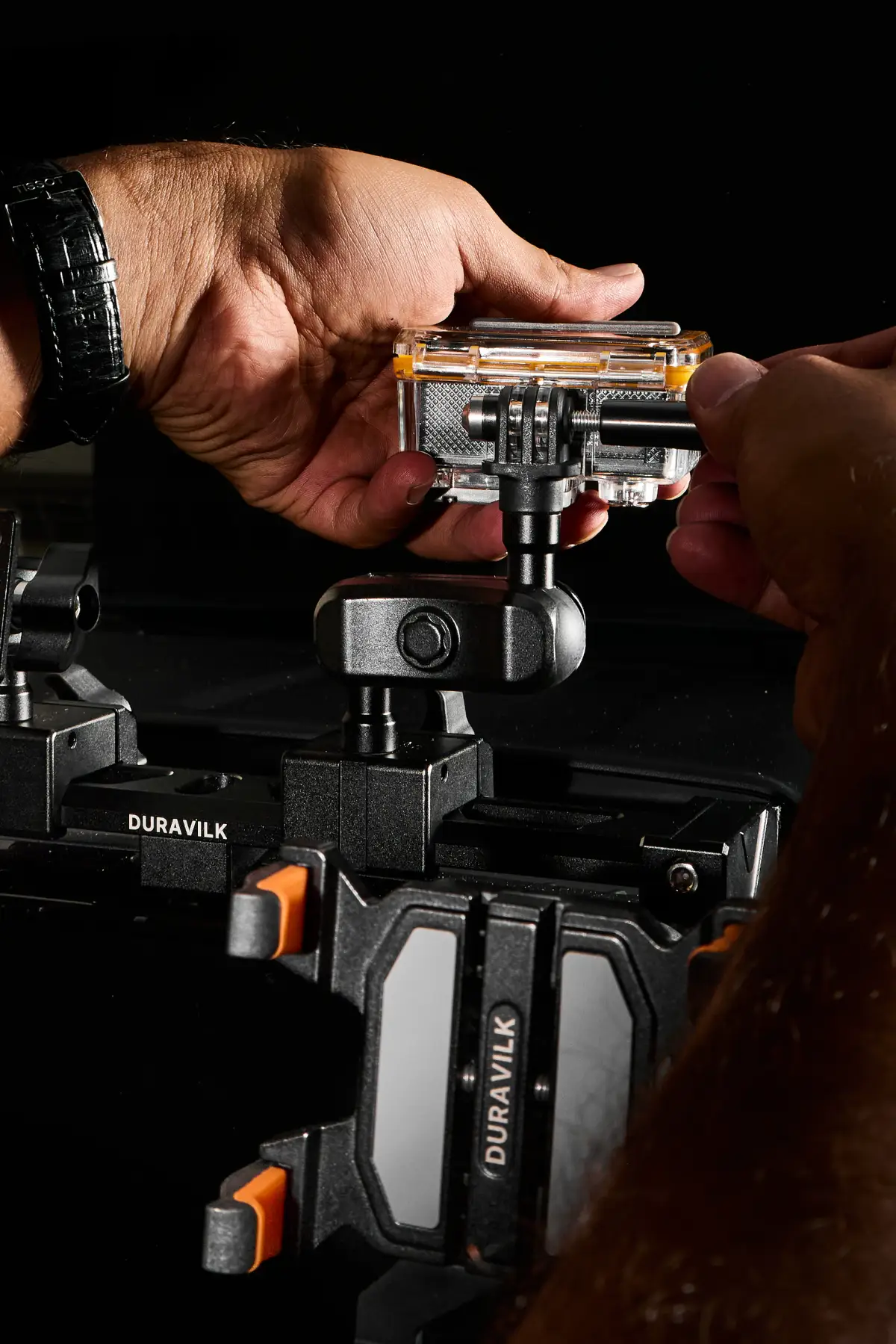 Hands working around an upper mount on the Duravilk rail above a branded device holder in a dark vehicle interior