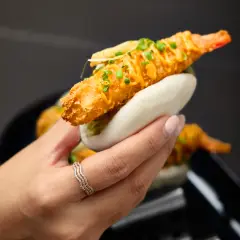 Handheld prawn bao with golden tempura, herbs, and soft bun photographed for Duxton Hotel Perth menu promotion.