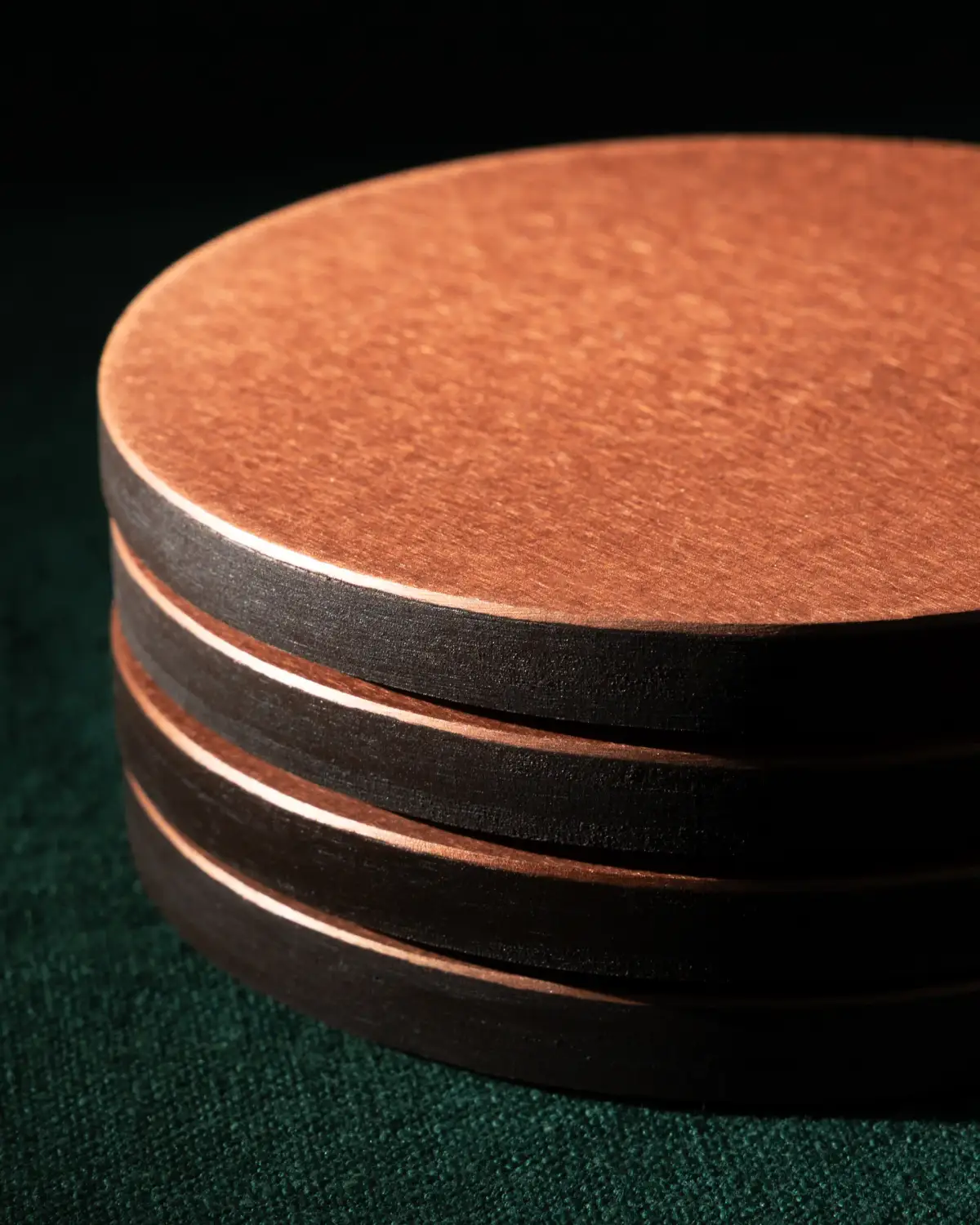 Copper coaster set photographed from above with a whisky glass, ice, and dried orange on a dark green surface
