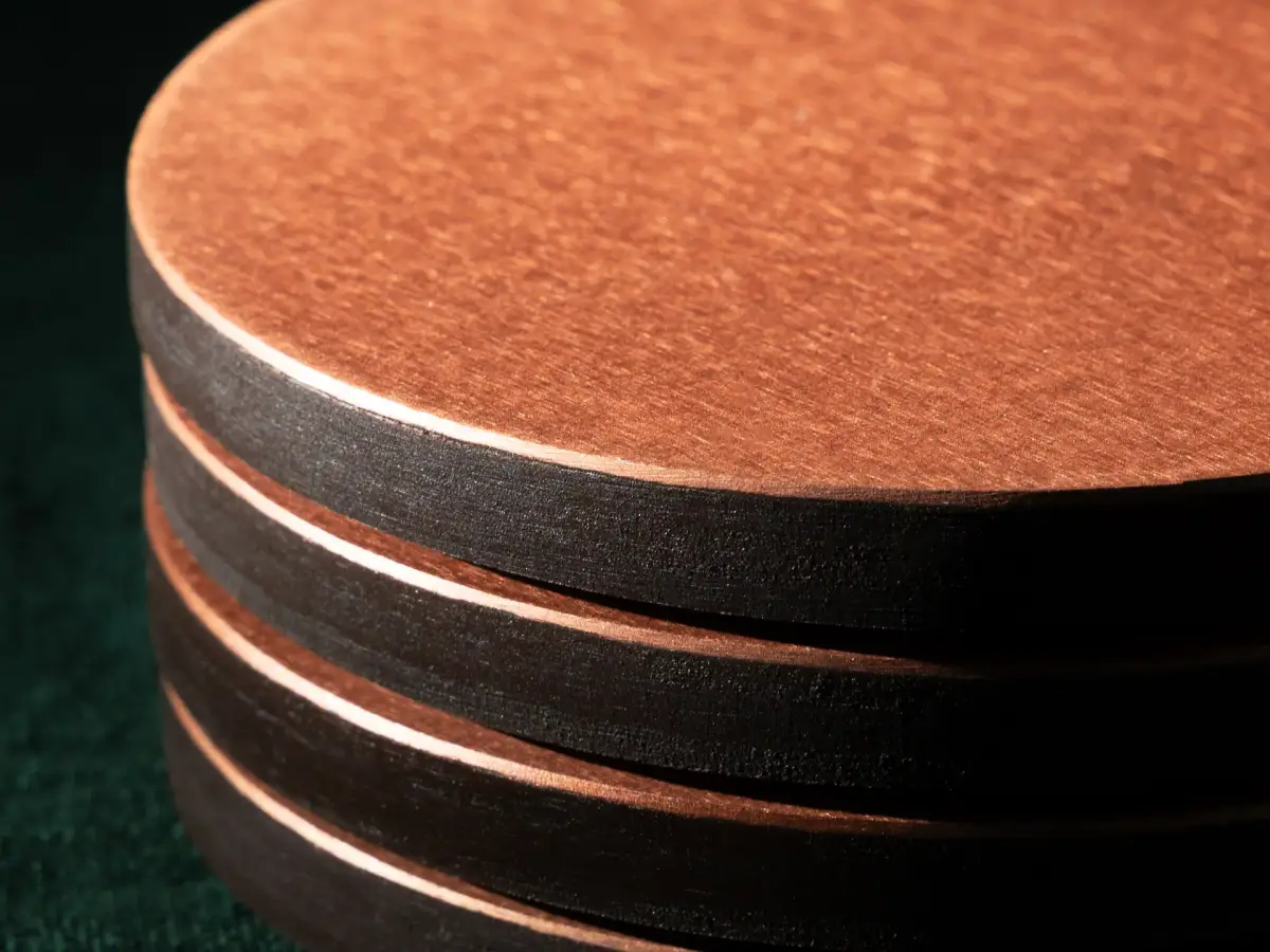 Copper coaster set photographed from above with a whisky glass, ice, and dried orange on a dark green surface