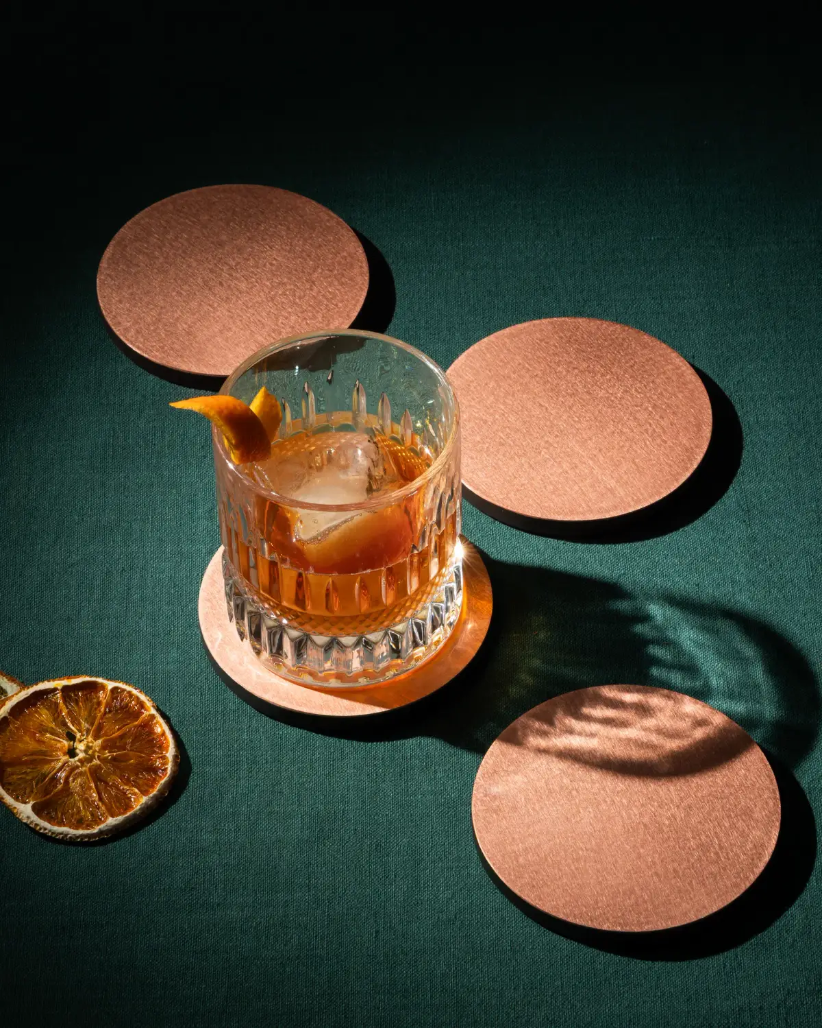 Old fashioned cocktail on a copper coaster with dried citrus garnish photographed in detail