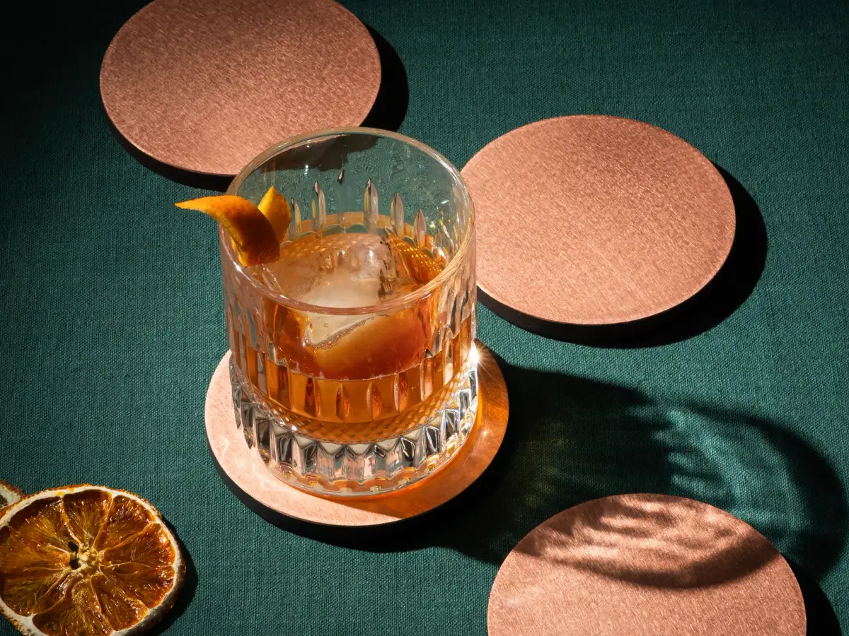 Old fashioned cocktail on a copper coaster with dried citrus garnish photographed in detail
