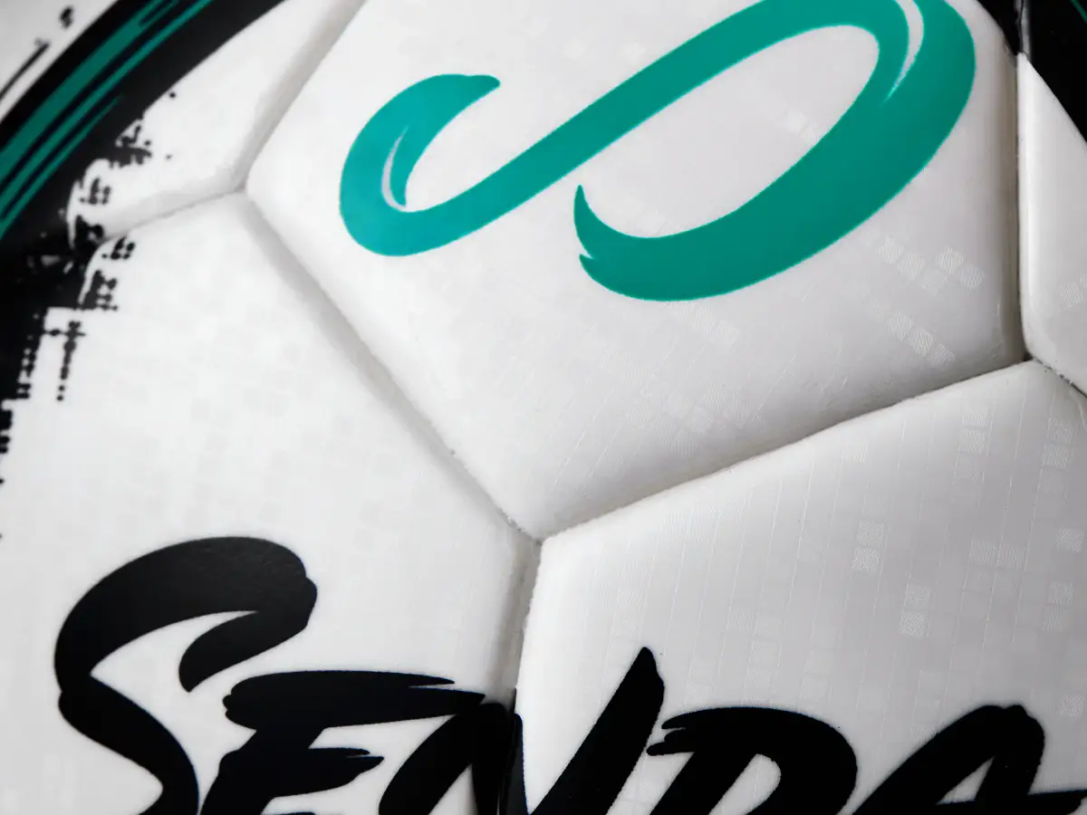 Macro product photograph of a Senda futsal ball showing the teal logo, printed graphics, and panel texture