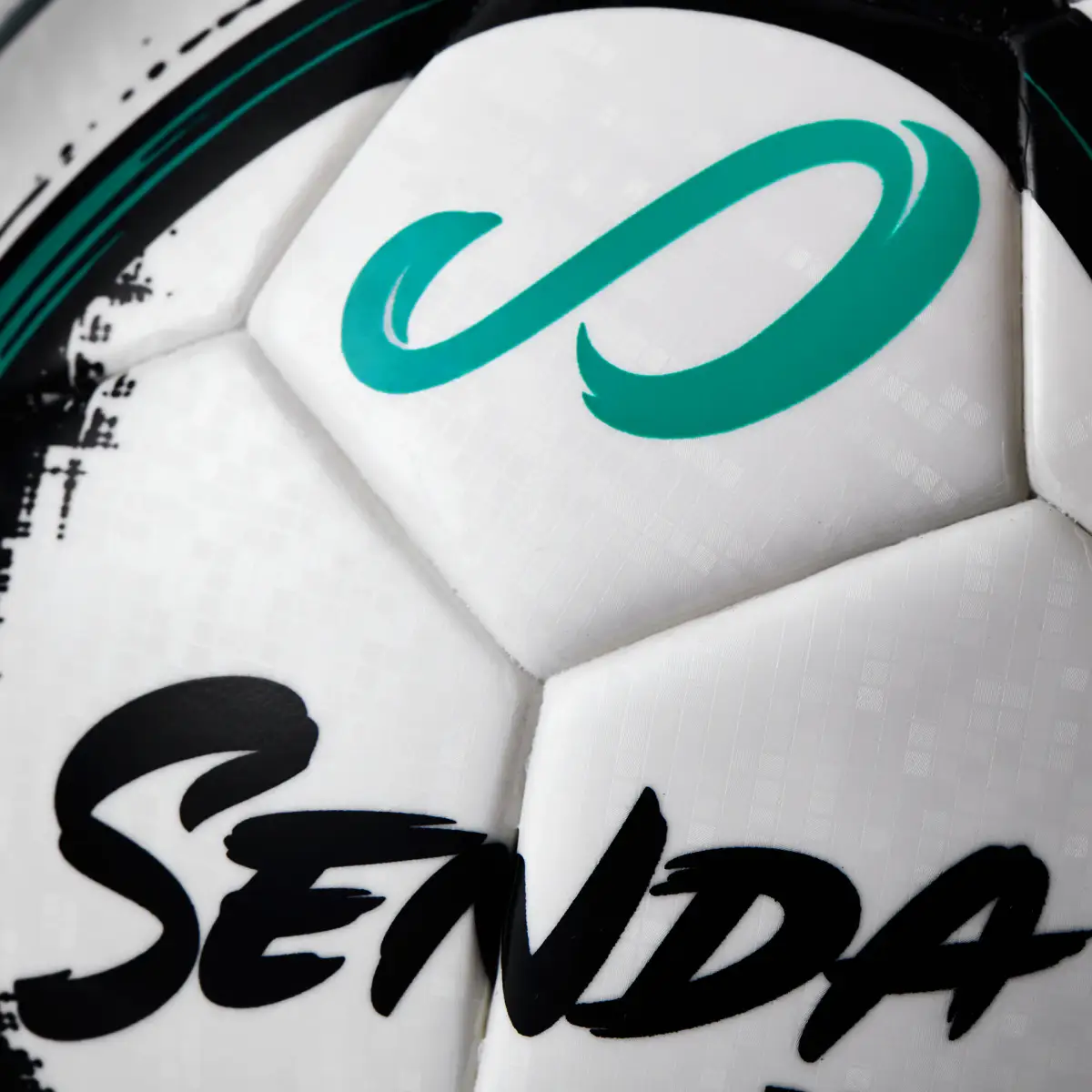 Macro product photograph of a Senda futsal ball showing the teal logo, printed graphics, and panel texture