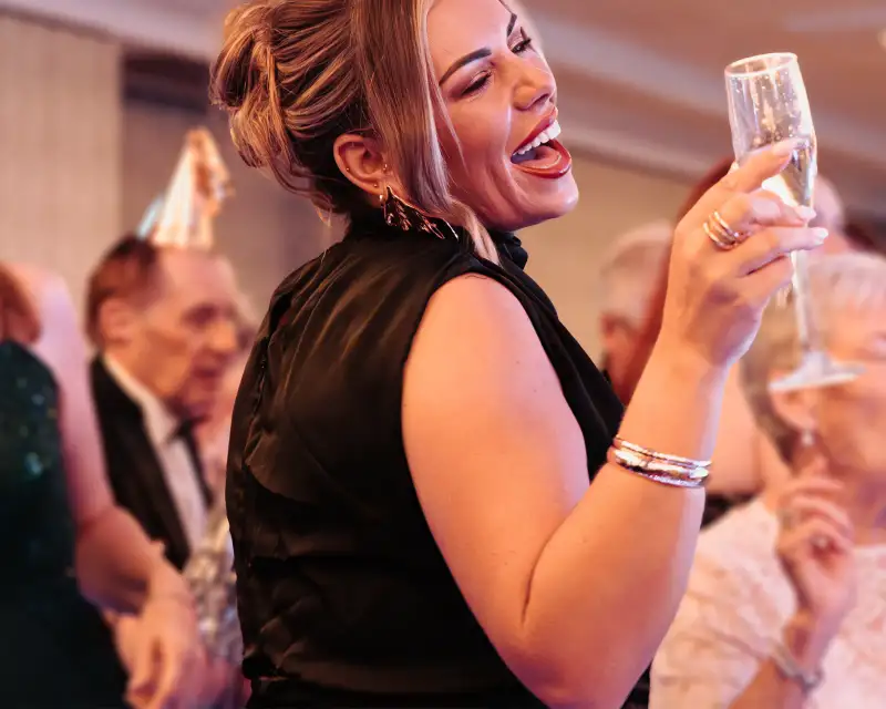 Candid event photography of a woman laughing with a glass of champagne at a function in Perth.