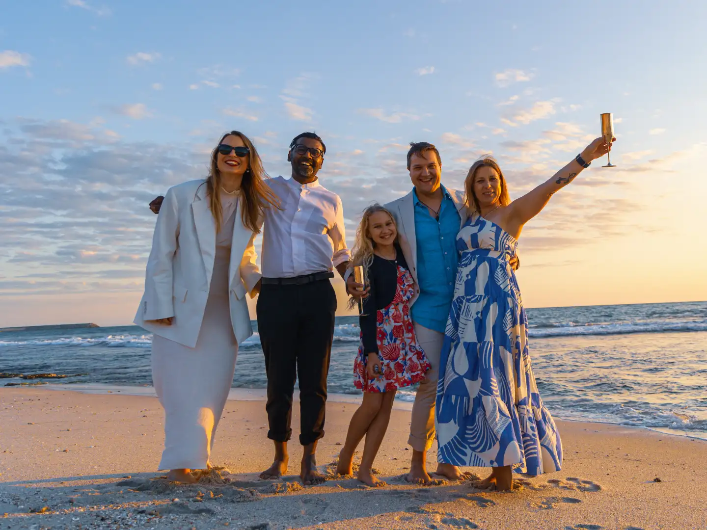 Family and friends raising a toast together on a Perth beach at sunset.
