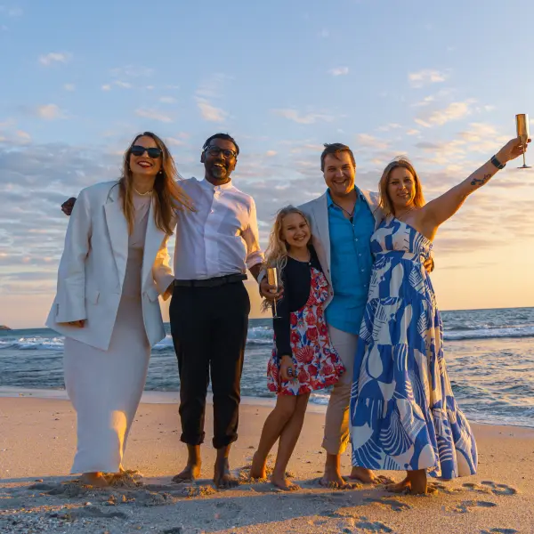 Family and friends raising a toast together on a Perth beach at sunset.
