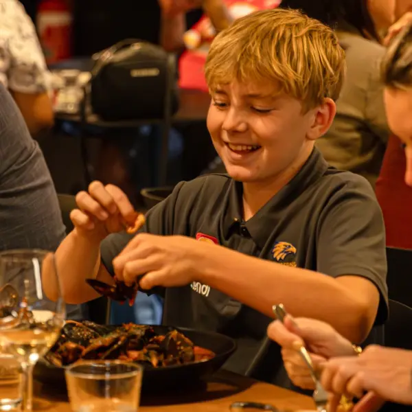 Smiling child eating mussels, capturing family-friendly dining atmosphere for Western Australia hospitality venues.
