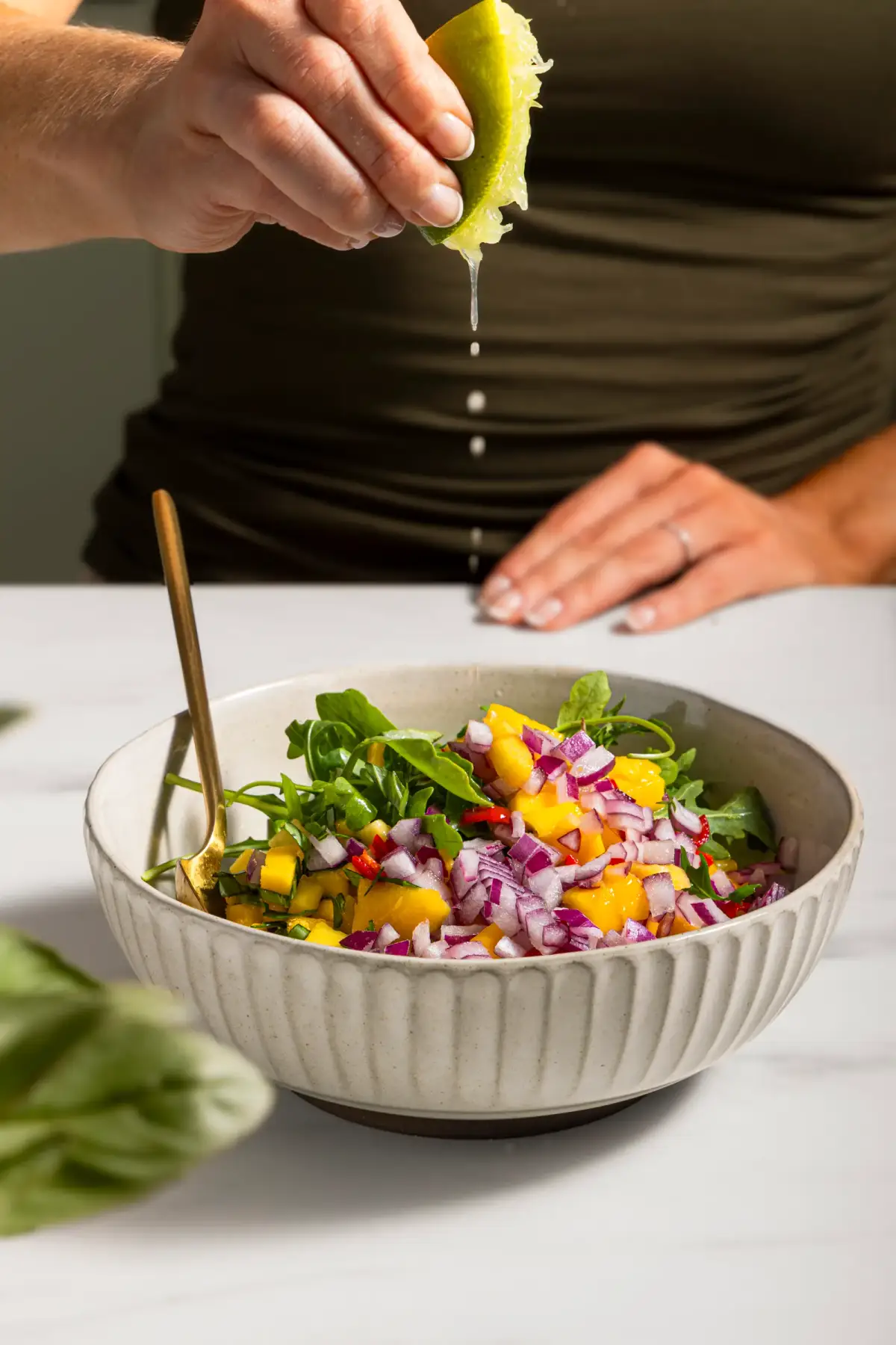 Lime juice being squeezed over a bowl of mango, red onion, and herb salad