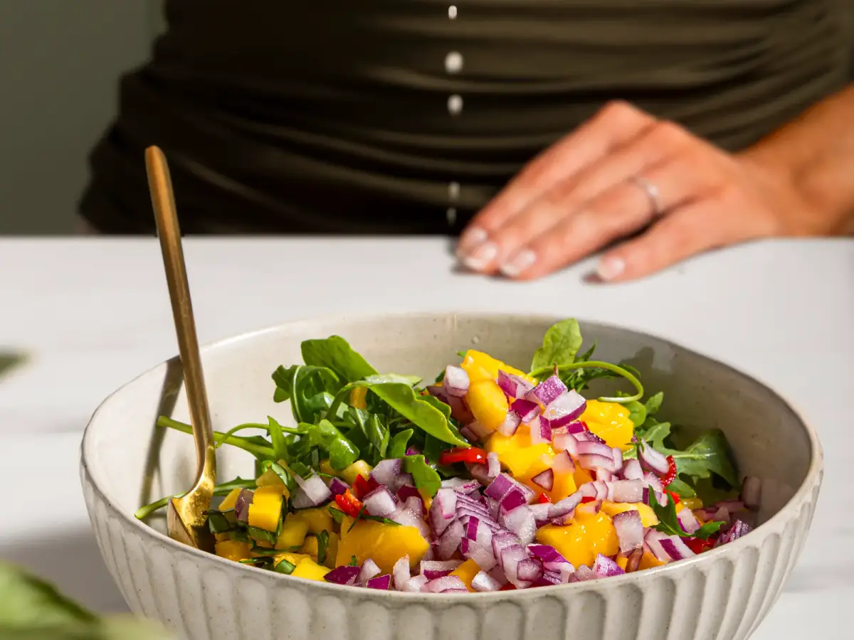Lime juice being squeezed over a bowl of mango, red onion, and herb salad