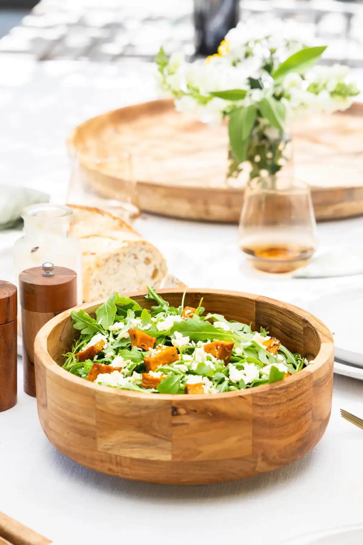 Wooden salad bowl filled with leafy greens, feta, and roast pumpkin on a bright styled table