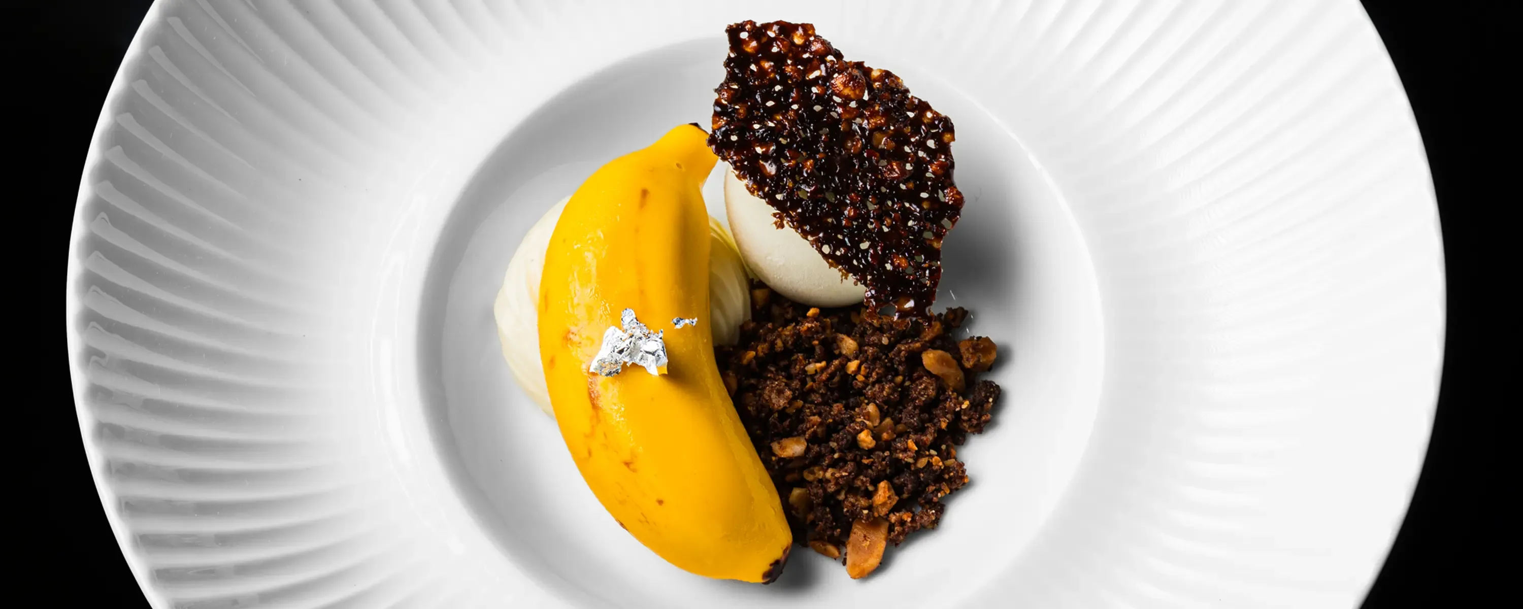 Artistic top-down shot of a gourmet yellow banana dessert and chocolate tuile for fine dining web design.