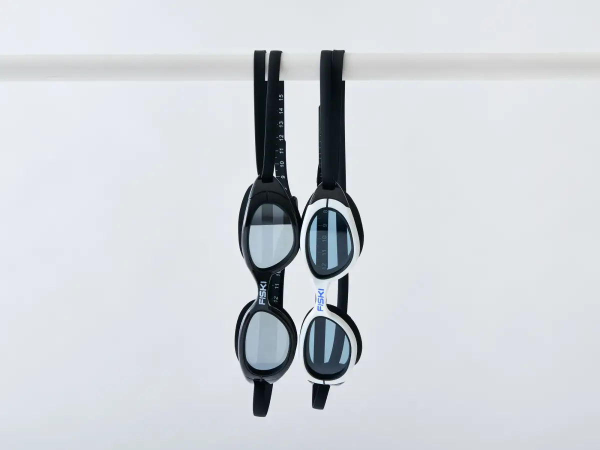 Black and white pairs of Fiski swimming goggles hanging side by side from a white rail showing the frame profile and lens shape