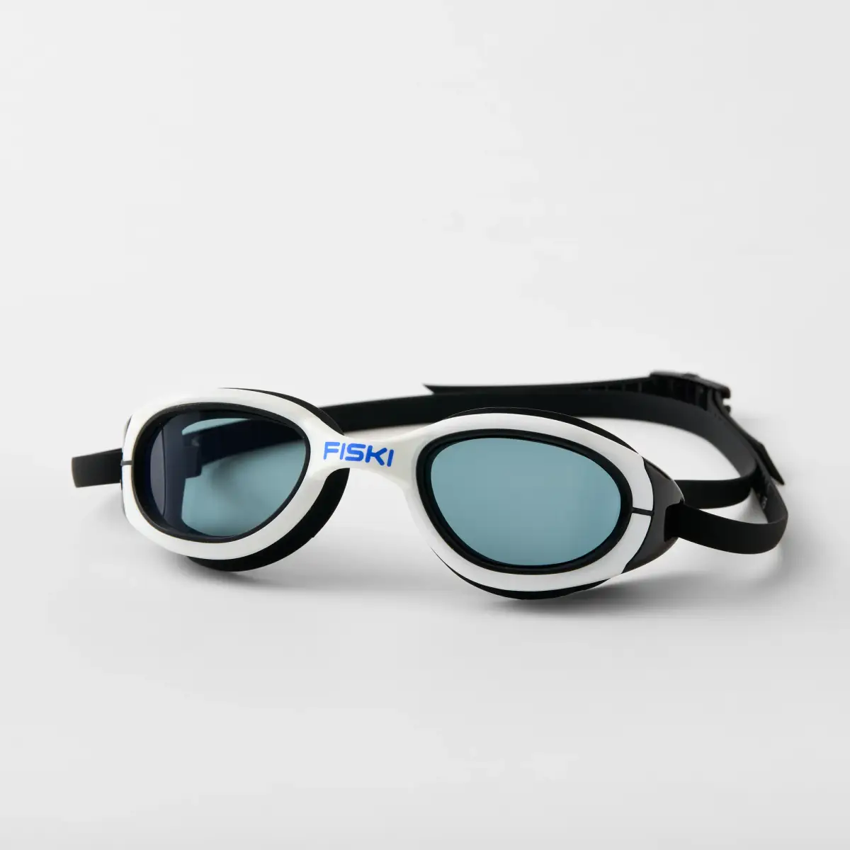 White and black Fiski swimming goggles with smoke tinted lenses and a black adjustable strap photographed on a white background
