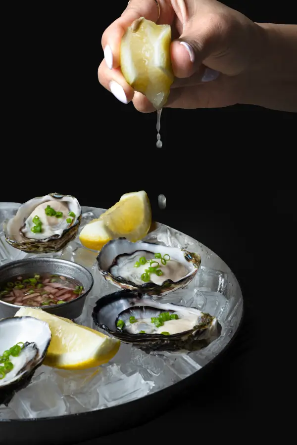 Fresh oysters with lemon being squeezed, action food photography for Perth seafood restaurants.
