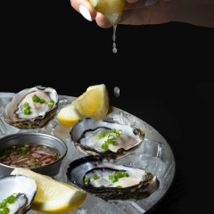 Hand squeezing fresh lemon over oysters on ice, dynamic seafood photography for Perth restaurant website hero banners.