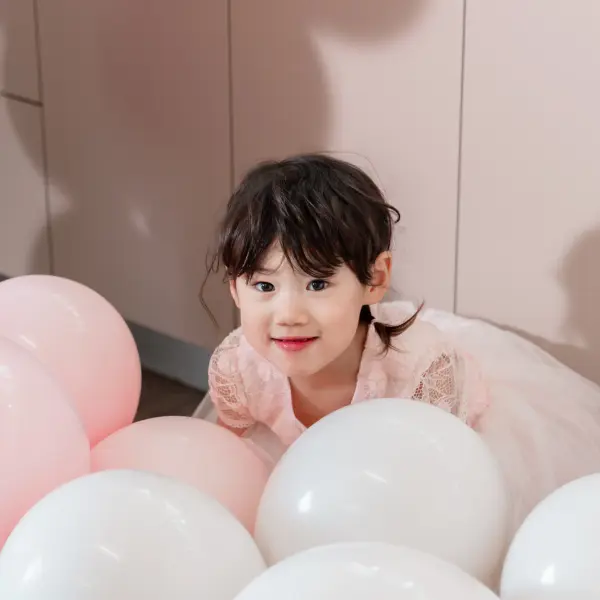 Child playing with pink balloons during a birthday party.
