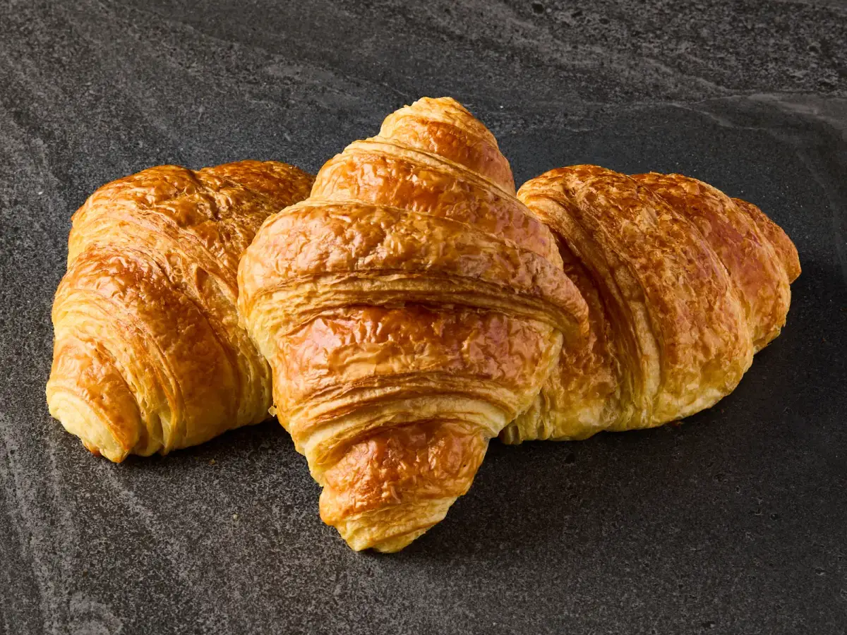 Three golden, flaky Il Granino butter croissants arranged on a dark stone surface for bakery product photography