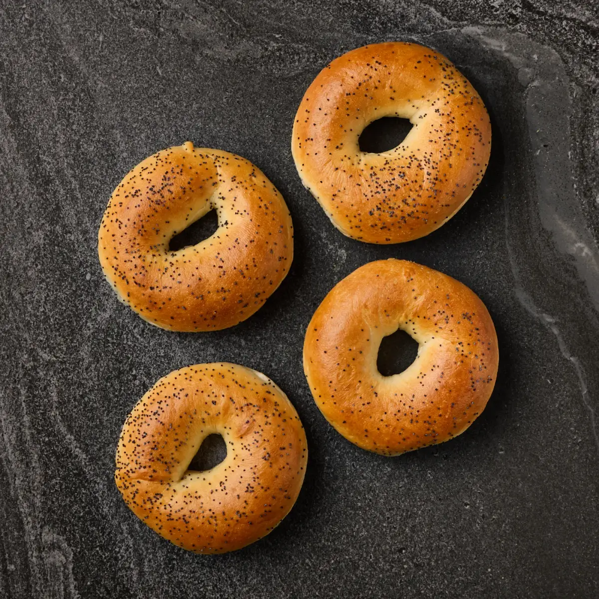 Four Il Granino poppy seed bagels photographed from above on a dark stone surface
