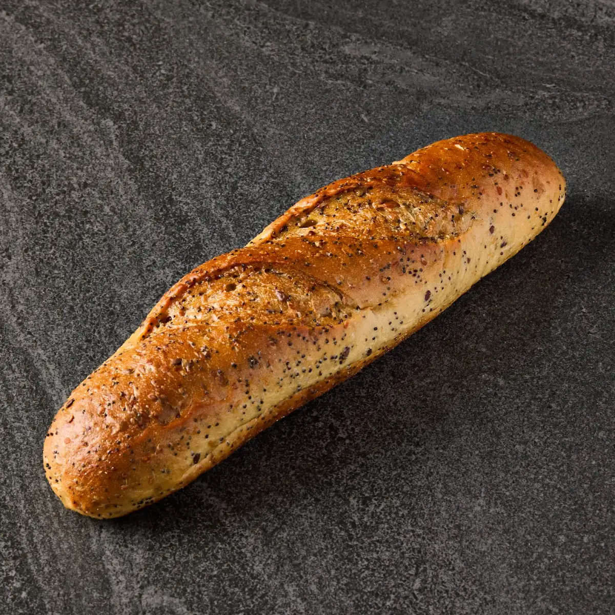 Single Il Granino seeded Vienna loaf with golden poppy seed crust on a dark stone surface