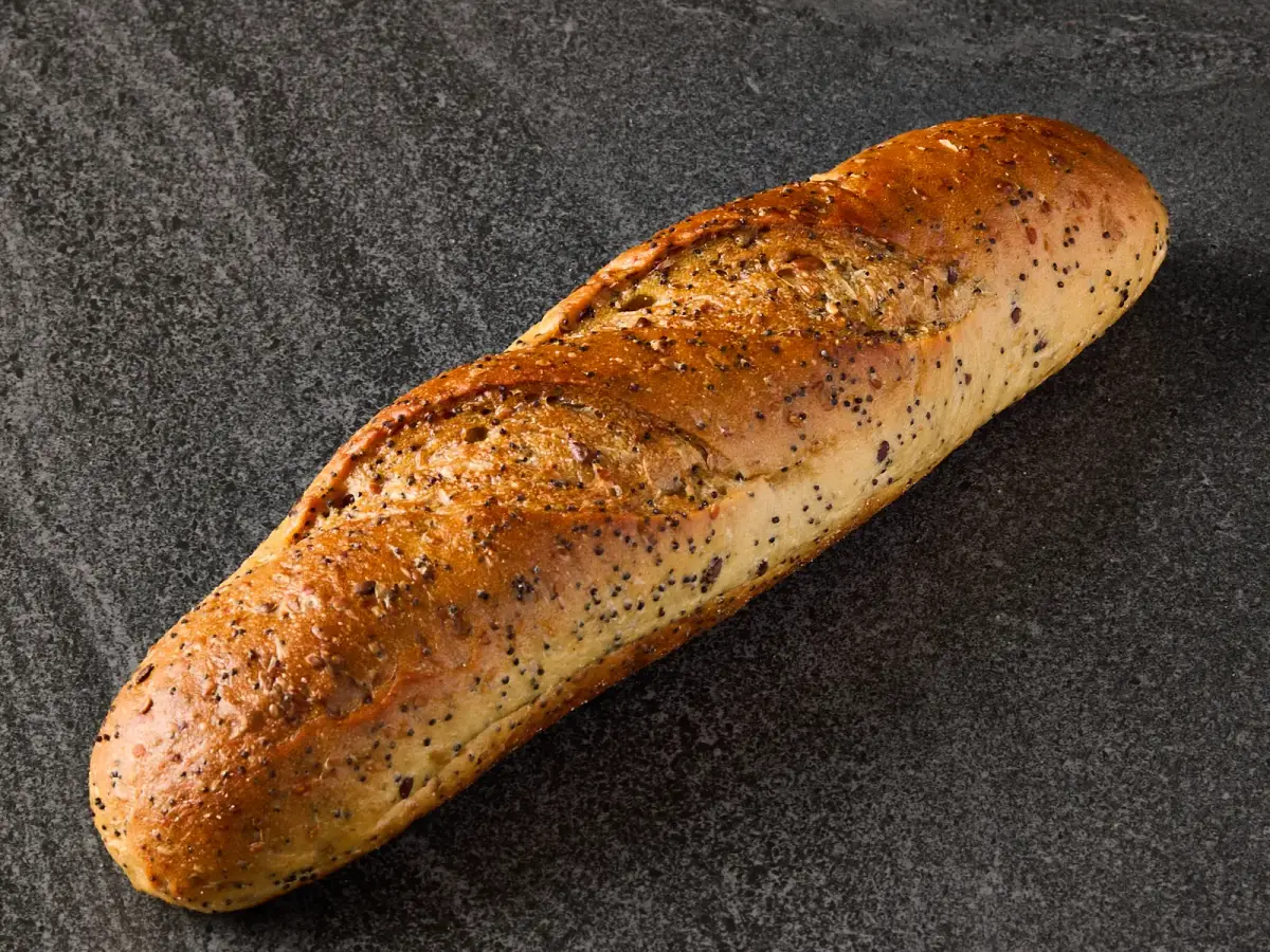 Single Il Granino seeded Vienna loaf with golden poppy seed crust on a dark stone surface