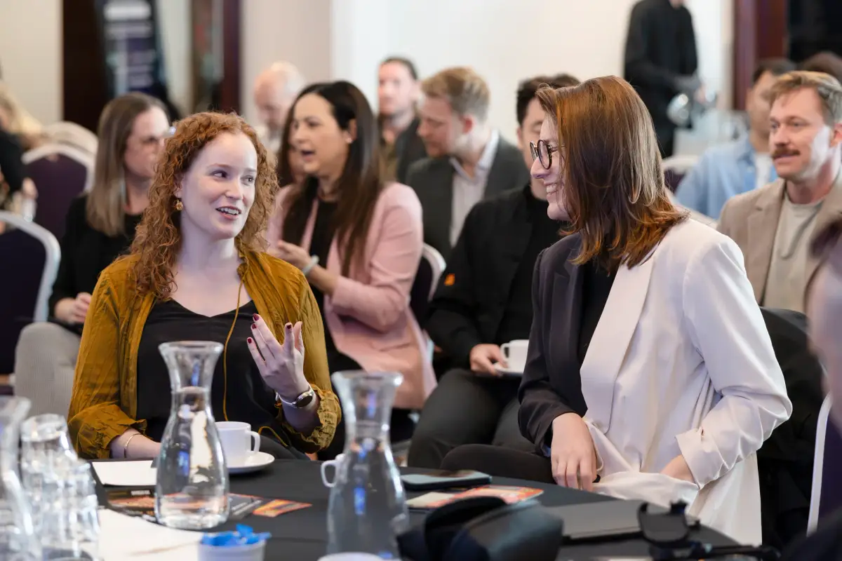 Two marketing professionals talking and laughing at a table during a break at the Intrigue MADVERSE Perth summit
