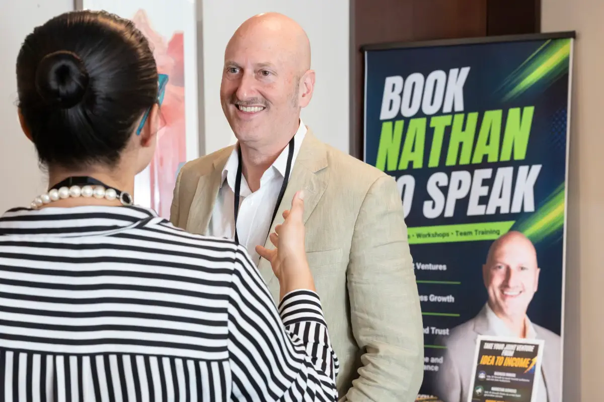 Speaker Nathan Baws talking with a delegate beside his banner at the Intrigue MADVERSE marketing summit in Perth