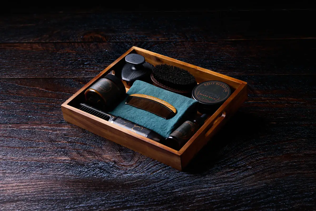Kelly Beard Co premium beard care kit arranged in a wooden tray with beard balm, beard oil, comb, brush, and grooming tools