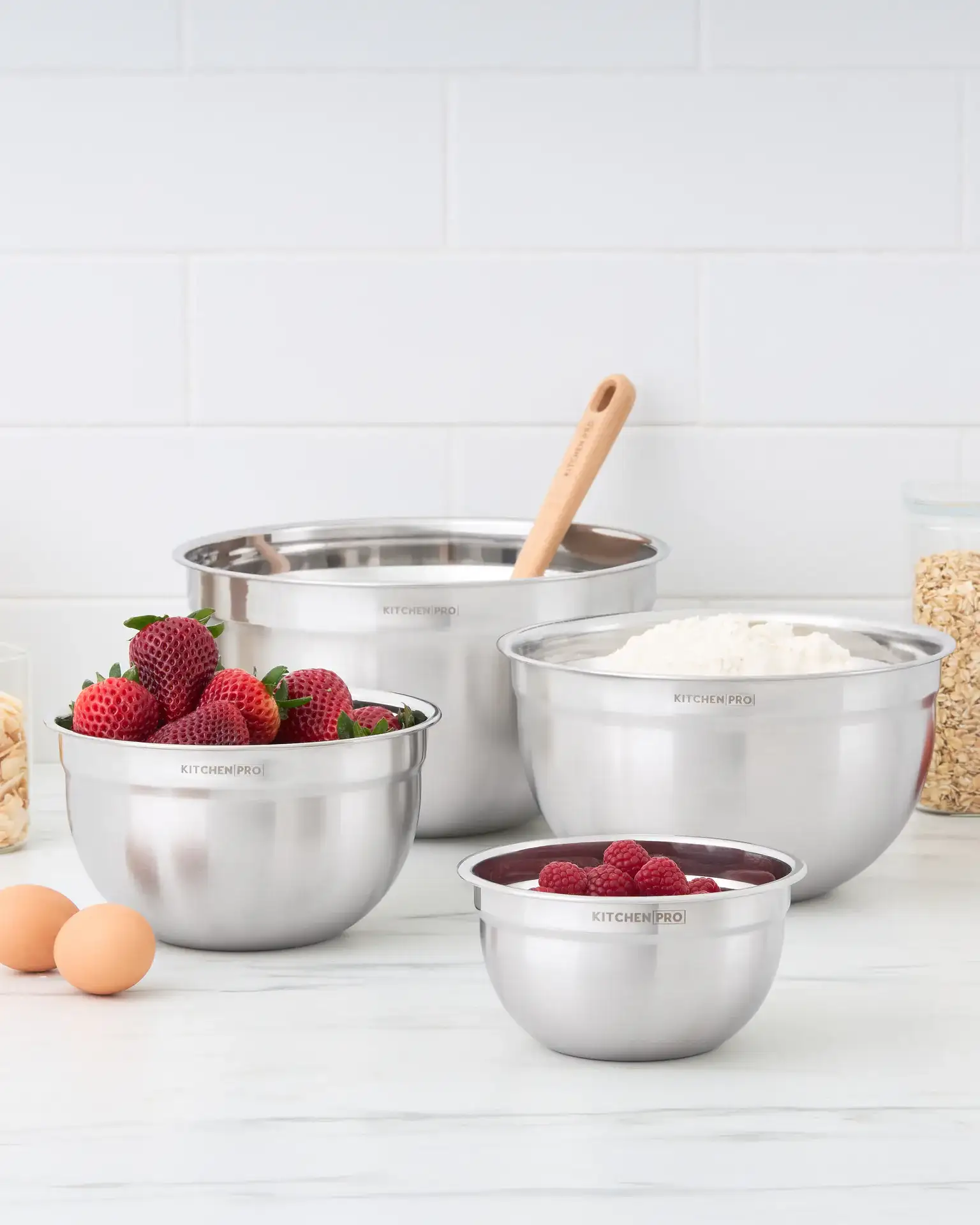 Kitchen Pro stainless-steel mixing bowl set styled with berries, flour, oats, almonds, and eggs in a bright kitchen by Jo-Anne Pabst