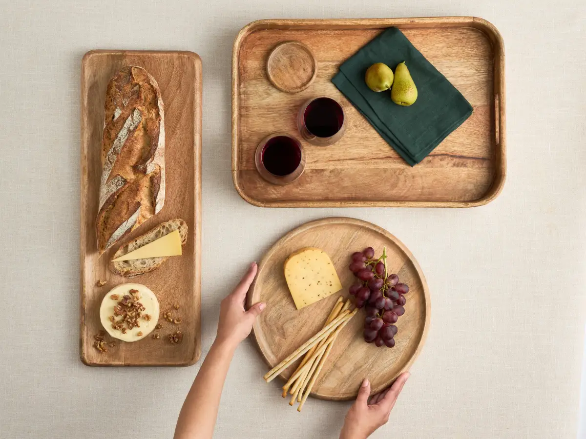 Overhead lifestyle photograph of Salisbury & Co Grove timber serving boards and trays styled with bread, cheese, fruit, and wine