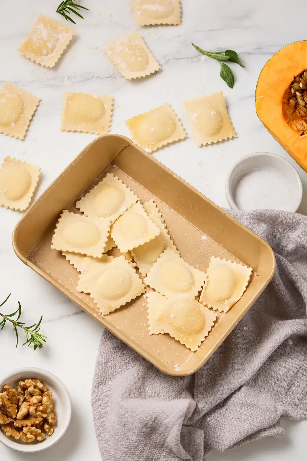 Fresh La Delizia Lab pumpkin ravioli arranged in a kraft tray with sage, walnuts, and a roasted pumpkin half on marble