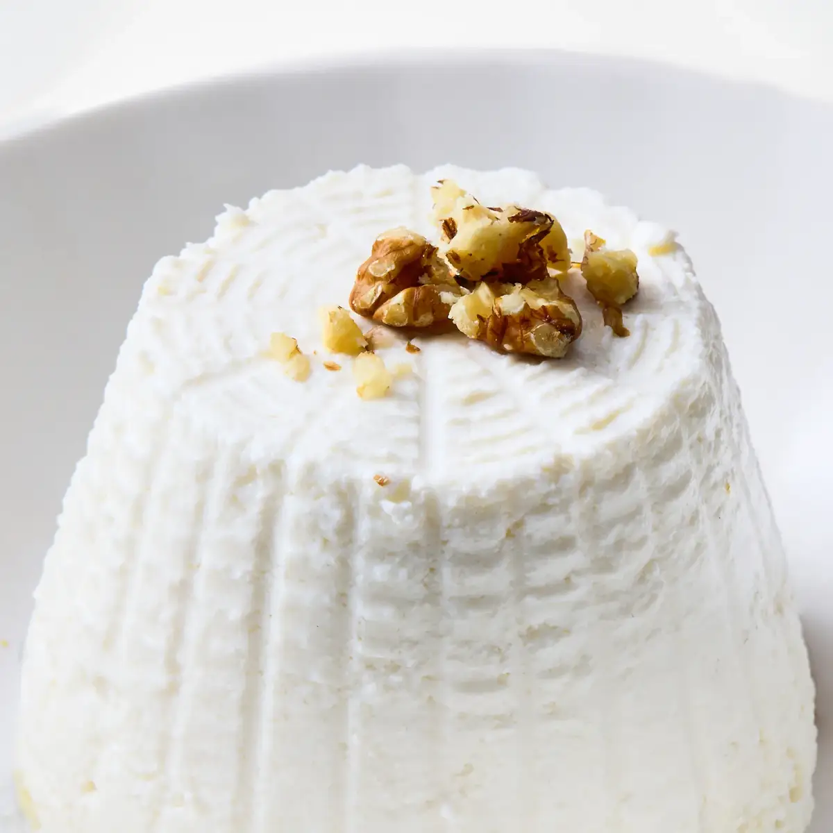 Close-up of La Delizia Latticini fresh ricotta topped with toasted pine nuts showing its soft, creamy texture