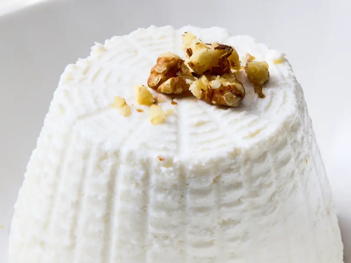 Close-up of La Delizia Latticini fresh ricotta topped with toasted pine nuts showing its soft, creamy texture