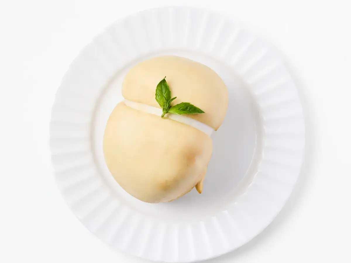 La Delizia Latticini smoked scamorza ball with golden rind and fresh basil on a white fluted plate