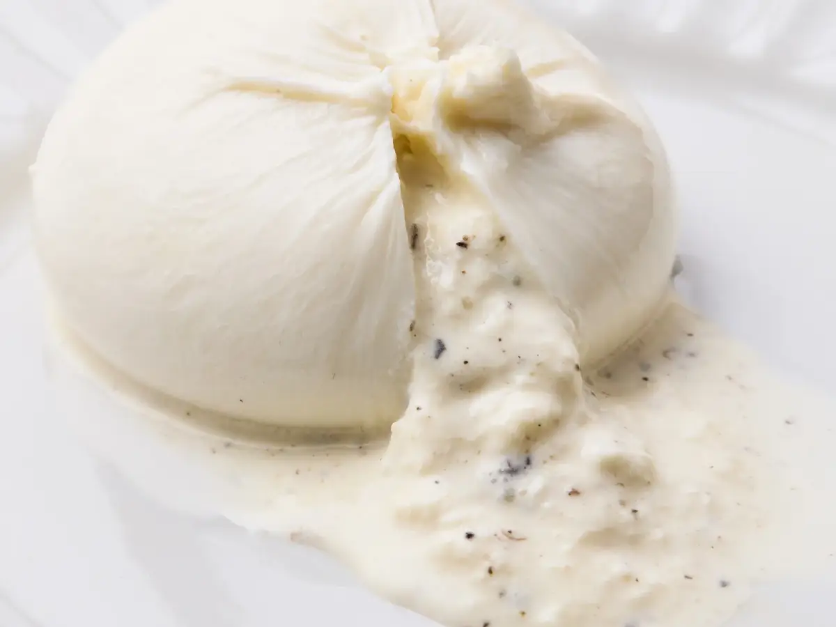 La Delizia Latticini truffle burrata cut open to show the creamy truffle-flecked stracciatella centre flowing onto the plate