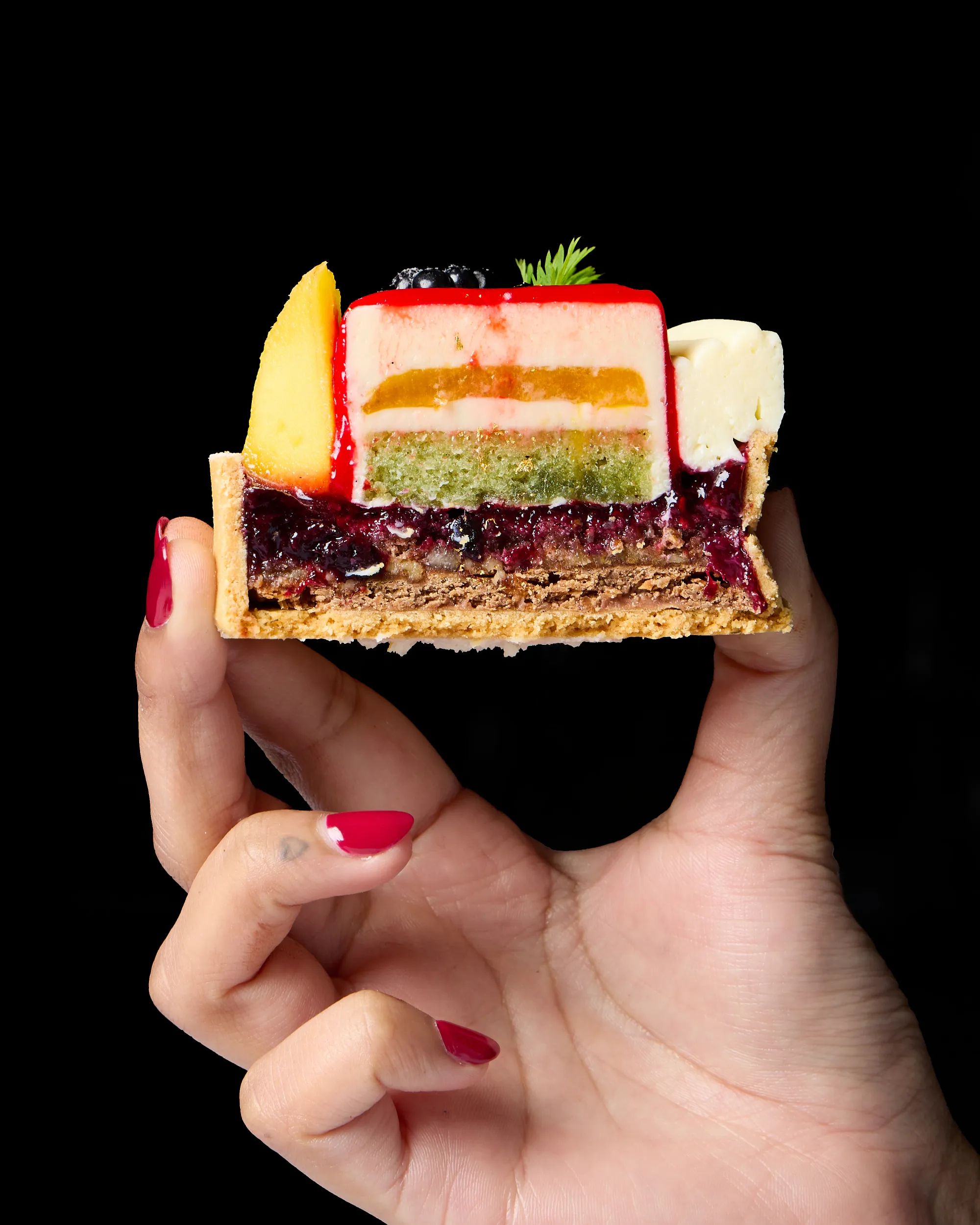 Layered pastry slice held in front of a dark background