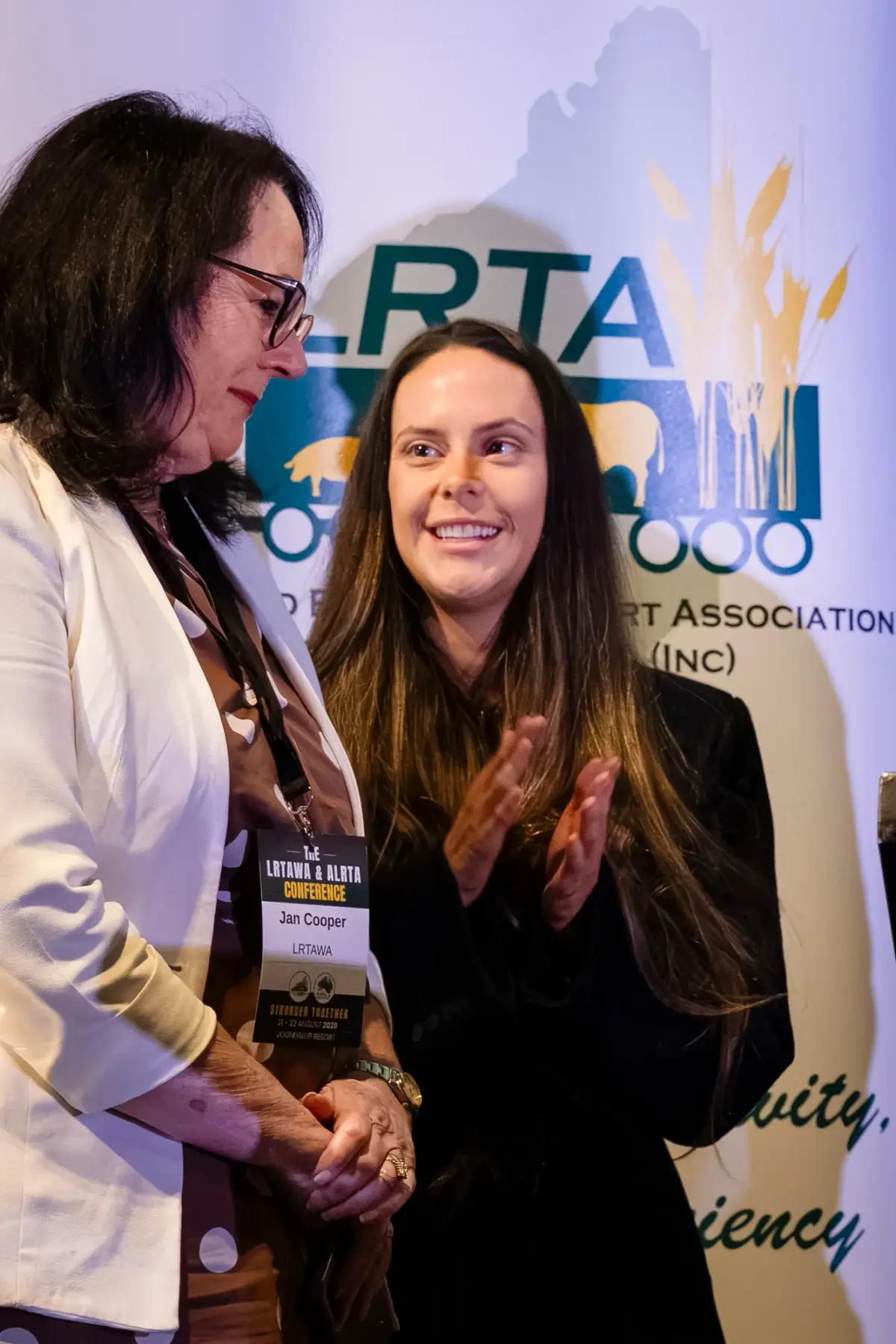 Two attendees beside an LRTAWA banner at LRTAWA Corporate Event.